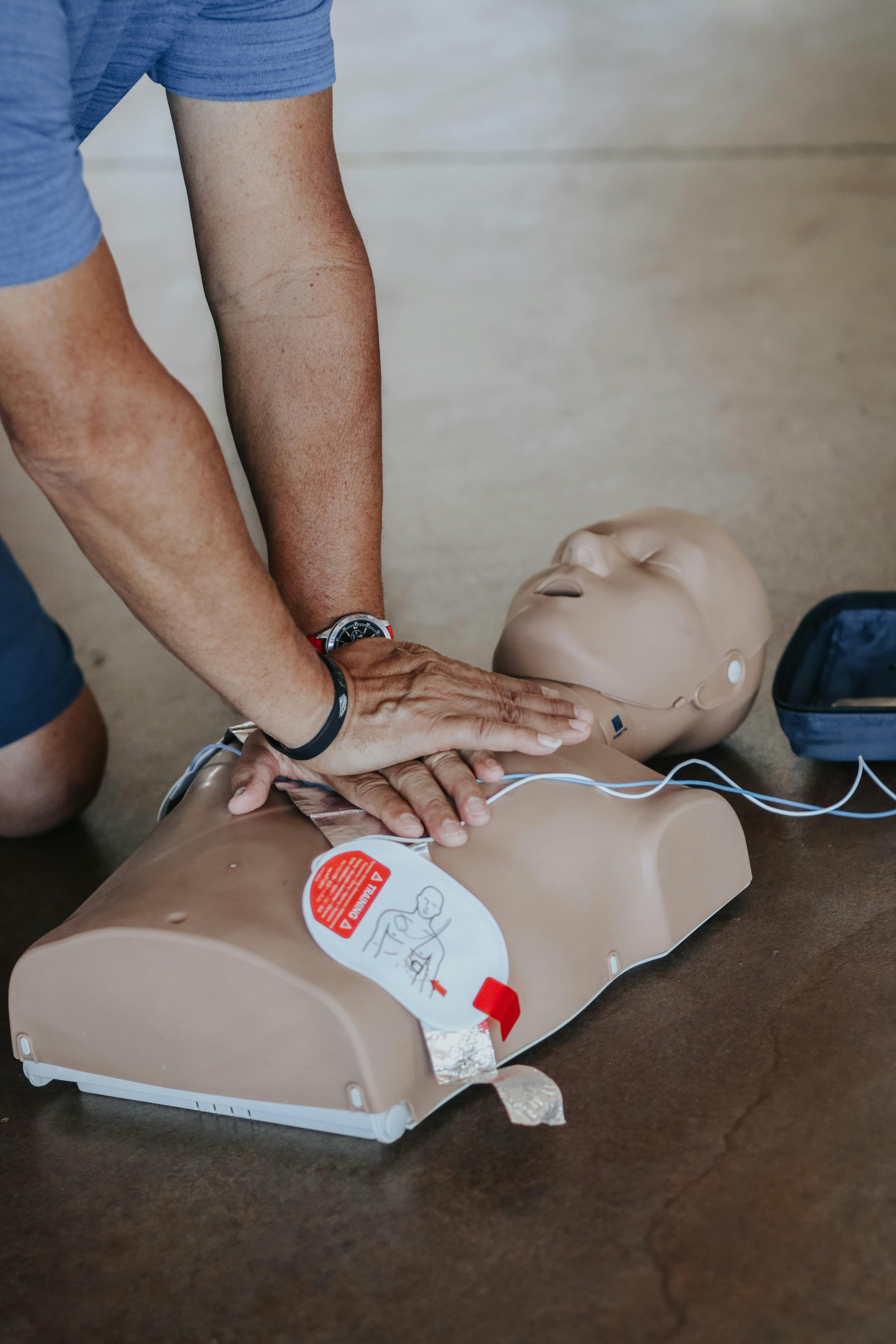 Instructor guiding first aid practice with manikin and AED trainer.
