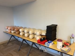 Training equipment lined up for an on-site class: manikins, AED trainers, and supplies.